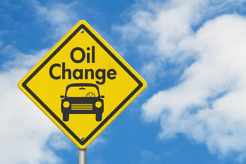 Oil change with car on yellow warning highway road sign with sky background