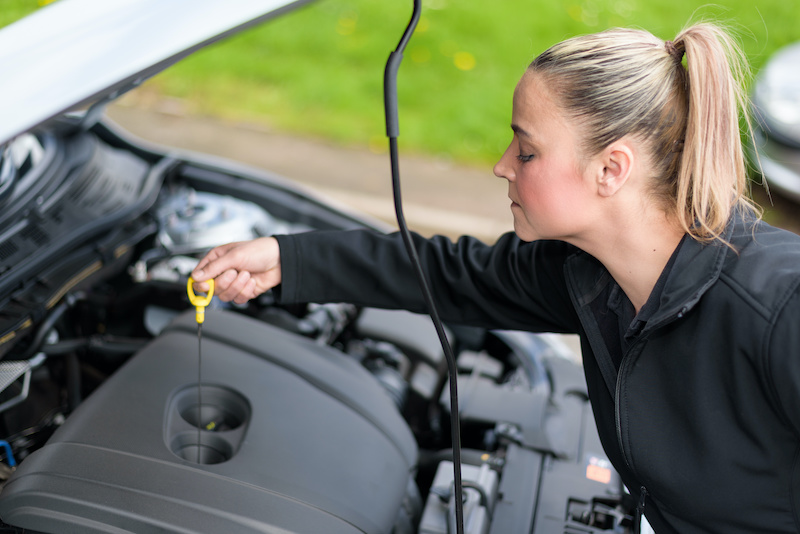 A woman mechanic checking a car's oil level at roadside
