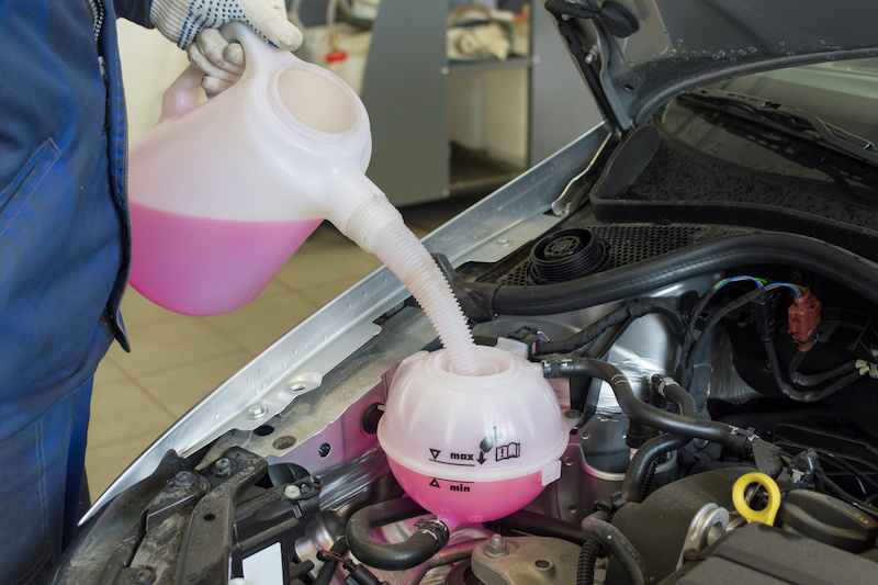 Car engine coolant expansion tank close-up. Professional mechanic pours antifreeze.