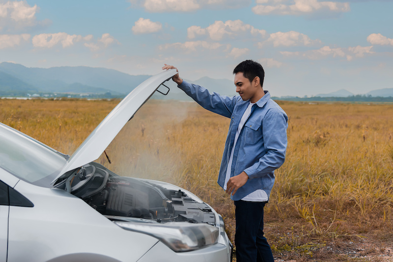 Overheated car and engine broke with breakdown radiator steam and hot oil smoke from under the hood. Asian young man auto driver standing open car hood on outdoors. Automobile motor problem concept.